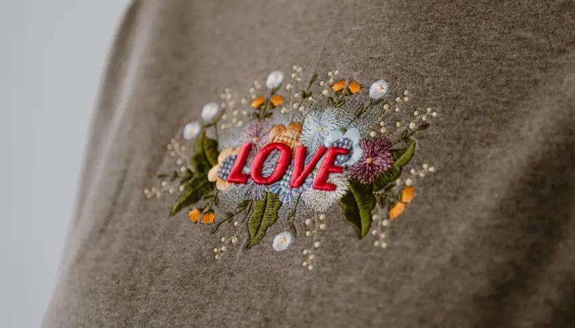 Besticktes Sweatshirt mit dem Wort "LOVE" umgeben von bunten Blumen. Zeigt, was man besticken kann.