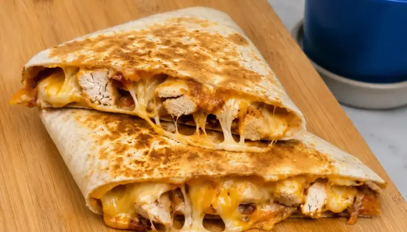 Pyszna quesadilla z kurczakiem, z ciągnącym się serem i kawałkami soczystego mięsa, podana na drewnianej desce.