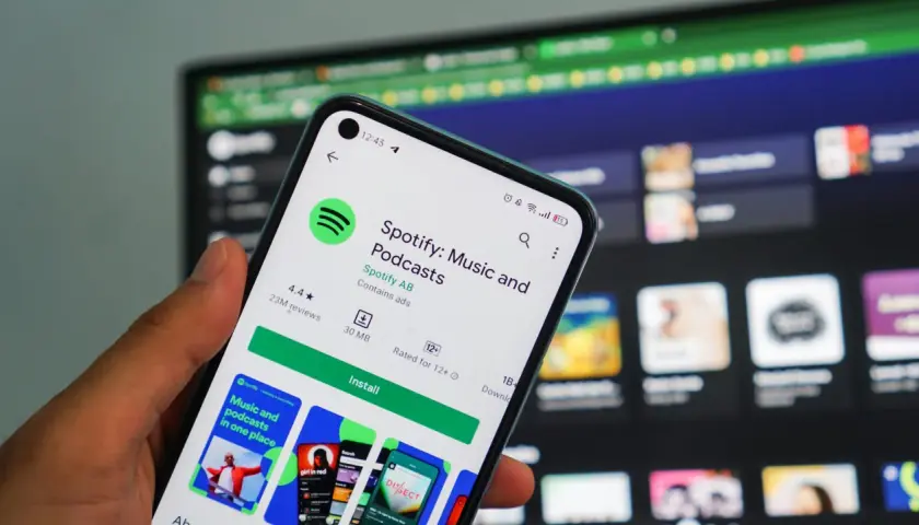 Dłoń trzyma smartfon z ekranem sklepu Google Play, gdzie widoczna jest strona aplikacji Spotify. To świetna okazja, by skorzystać z **spotify promocja** i pobrać ulubioną muzykę i podcasty.