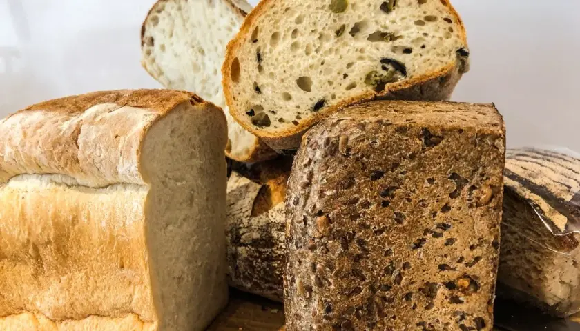 Różnorodne pieczywo, w tym bochenek z ziarnami i kromka z oliwkami. Czy chleb żytni ma gluten? Tak, większość chlebów, w tym żytni, zawiera gluten.