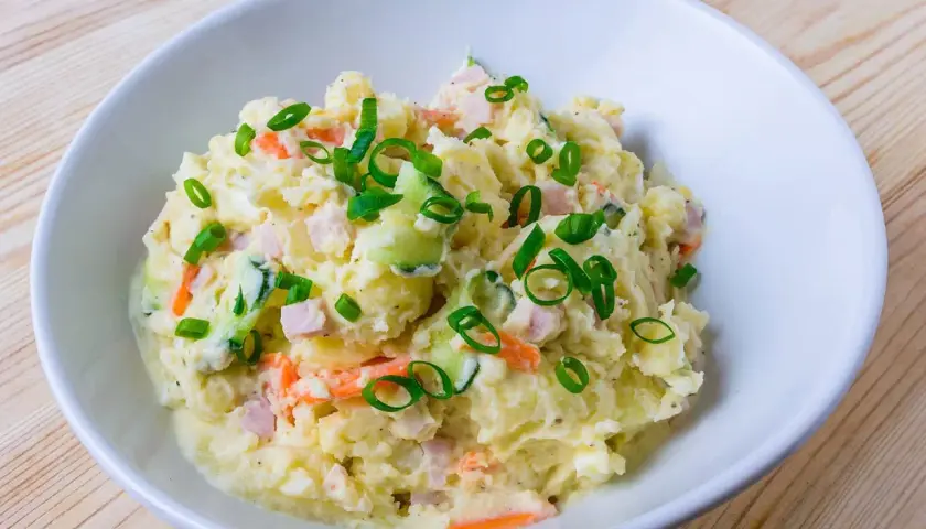 En skål med krämig potatissallad, toppad med purjolök. Den här ser ut att vara den godaste potatissalladen!