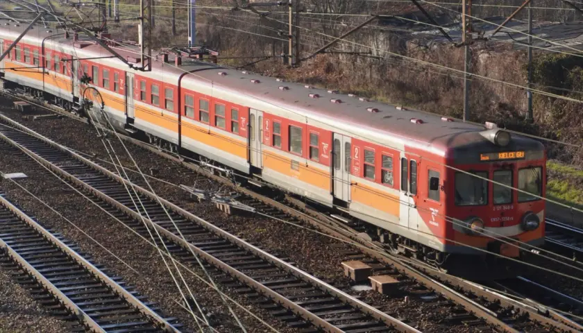 Czerwono-pomarańczowy pociąg elektryczny EN57 na torach.