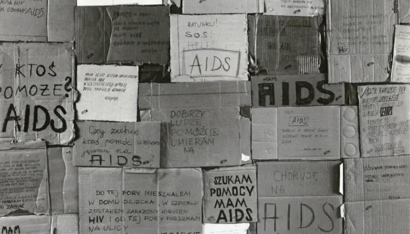 Ludzie błagają o pomoc, umierają na AIDS. Kartony z napisami "SOS", "Help", "Proszę o pomoc" świadczą o desperacji i walce o życie w obliczu choroby, która w tamtych czasach była naznaczona stygmatyzacją i brakiem wsparcia, tworząc swoistą **hegemonię*...
