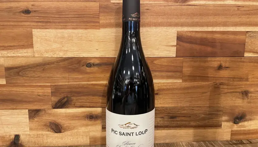 Bouteille de vin rouge du domaine Pic Saint Loup, "Réserve Les Almadies", sur fond de bois.