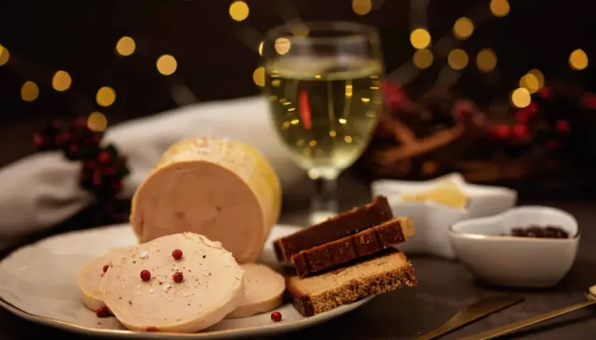 Tranche de vin foie gras sur une assiette, avec du pain d'épices et un verre de vin blanc. Ambiance festive.
