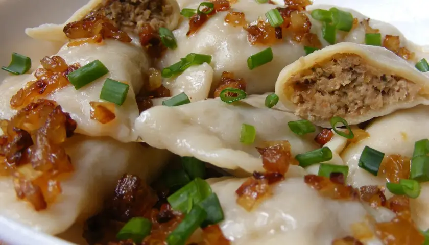 Pierogi z mięsem posypane skwarkami i szczypiorkiem.