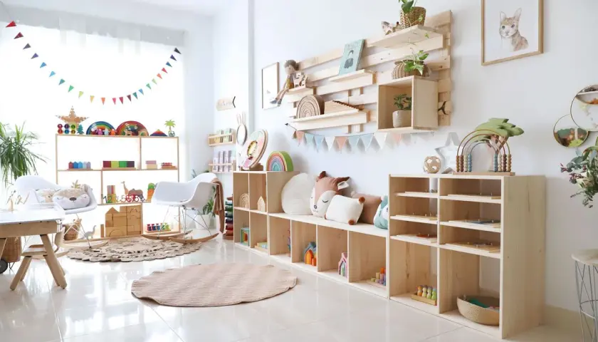 Acogedor rincón de juegos en el salón, con estanterías de madera llenas de juguetes educativos, cojines y una alfombra circular.