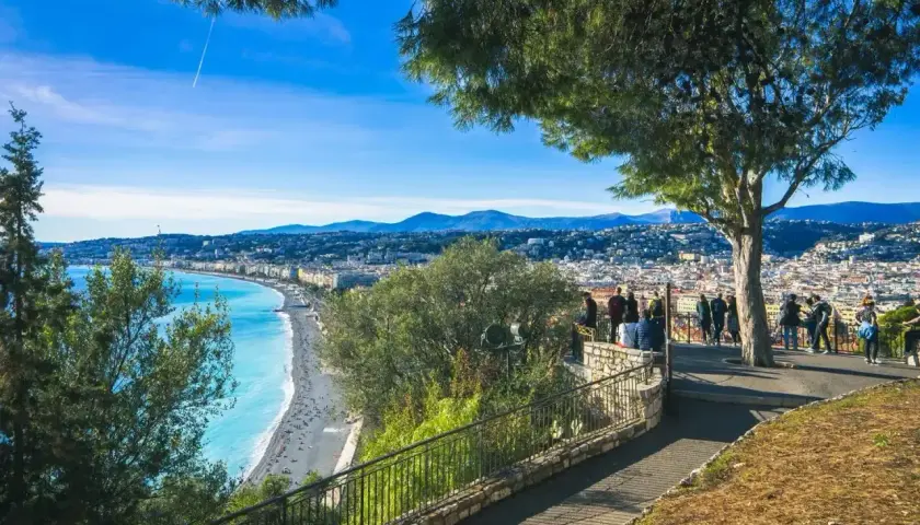 Widok na lazurowe morze i Niceę, stare miasto z promenadą. Ludzie podziwiają panoramę z tarasu widokowego.