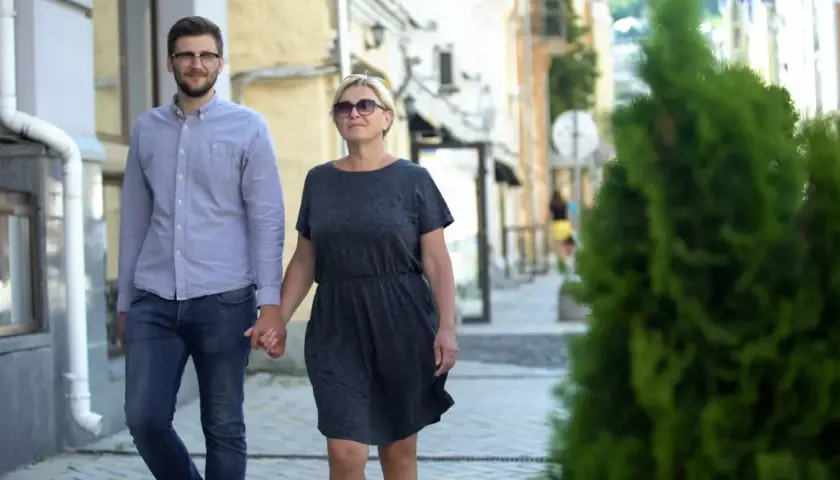 Para spaceruje ulicą, trzymając się za ręce. Młodszy mężczyzna w okularach i starsza kobieta pokazują, że różnica wieku w związku nie jest przeszkodą.