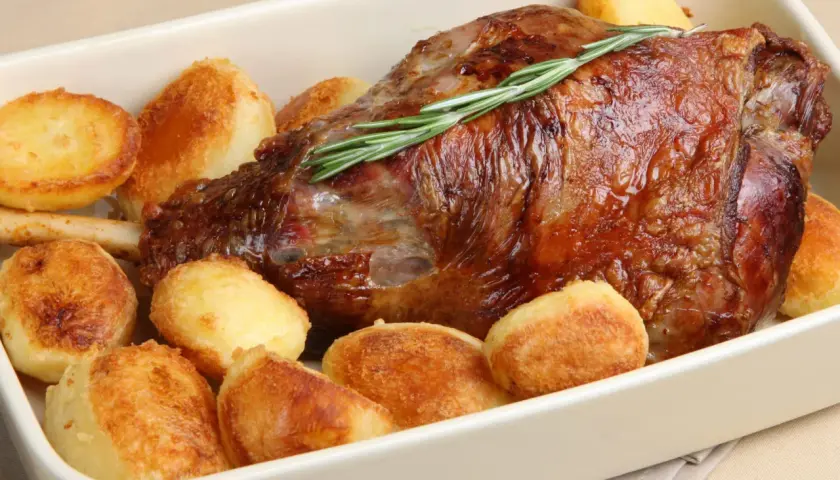 Gigot d'agneau rôti, garni de romarin, entouré de pommes de terre au four dorées et croustillantes. Un plat savoureux prêt à être dégusté.