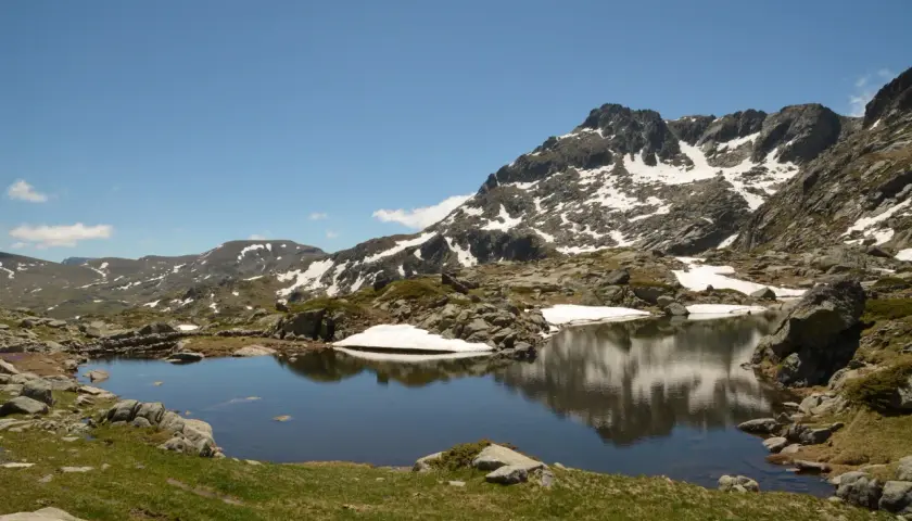 Góry Pirin z jeziorem odbijającym skaliste szczyty i resztki śniegu.