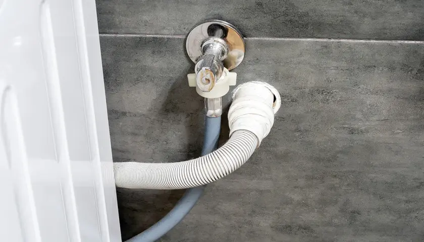 Instalacja odpływu do pralki. Wąż odpływowy podłączony do syfonu pod zlewem, na odpowiedniej wysokości.
