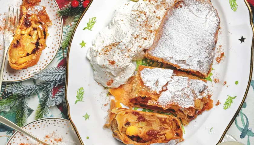 Delizioso strudel di mele con pasta sfoglia, cosparso di zucchero a velo e servito con panna montata e cannella.