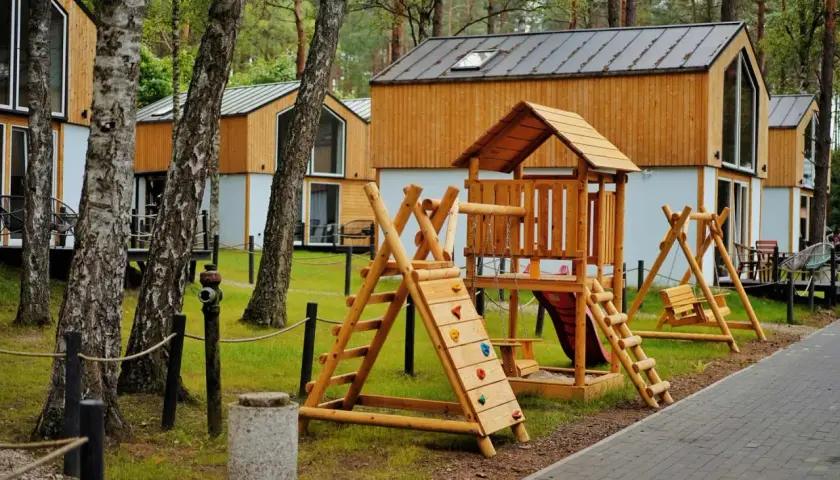 Drewniany plac zabaw z domkami w tle. Idealne bory tucholskie atrakcje dla dzieci, gdzie można odpocząć i bawić się na świeżym powietrzu.