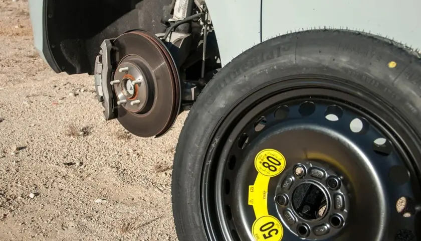 Rueda de galleta de repuesto junto al disco de freno de un coche, lista para ser instalada.