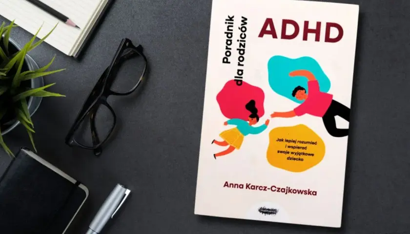 Książka "ADHD. Poradnik dla rodziców" Anny Karcz-Czajkowskiej, z ilustracją rodzica i dziecka. Obok notatnik, okulary i długopis.