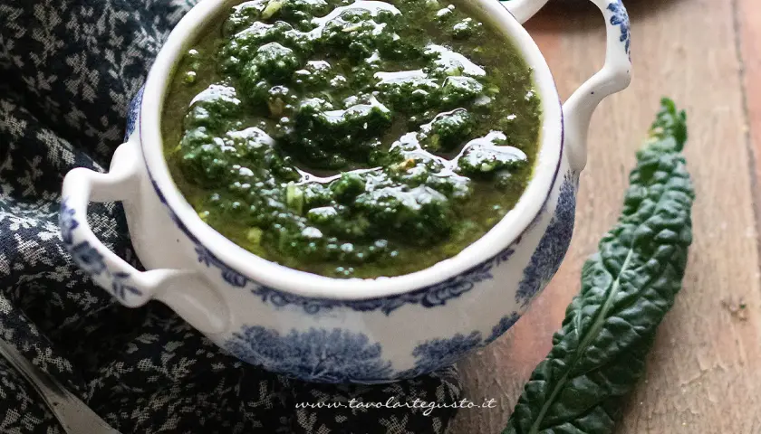 Pesto di cavolo nero in una ciotola decorata, accanto a una foglia fresca. Un condimento sano e saporito.
