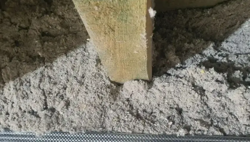 Drewniana belka w luźnej, szarej masie. To celuloza ocieplenie, które zapewnia komfort termiczny.