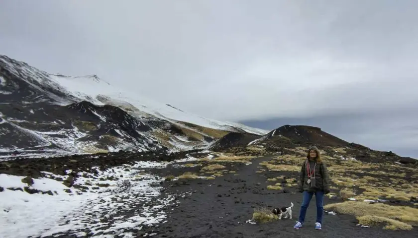 Una donna e il suo cane esplorano il paesaggio lunare dell'Etna in Sicilia, con neve e rocce vulcaniche.
