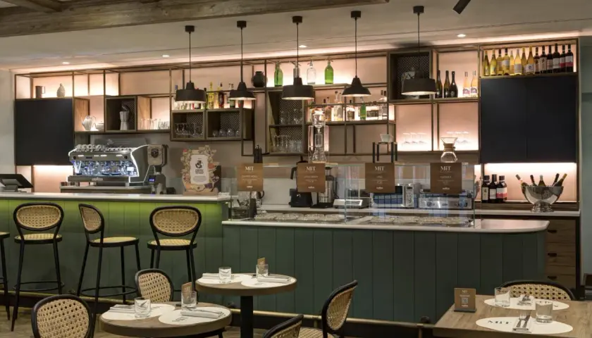 Interno di un locale moderno con bancone, macchine da caffè e tavoli. Un'atmosfera perfetta per gustare un ottimo caffè a Roma, famoso in tutto il mondo.