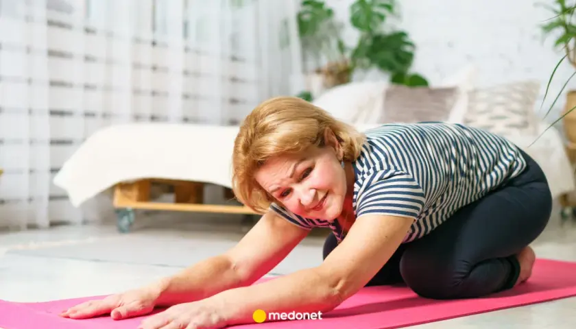 Starsza kobieta wykonuje ćwiczenia na osteoporozę na różowej macie w domu.