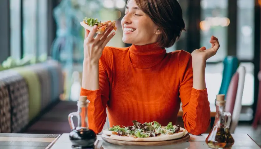 Kobieta w pomarańczowym golfie delektuje się pizzą, czując przypływ seratoniny.