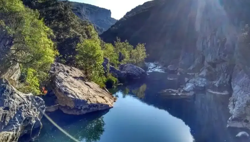 El río fluye sereno en la Foz de Lumbier, rodeado de imponentes rocas y vegetación exuberante bajo un sol radiante.