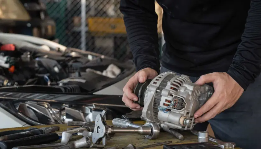 Mechanik trzyma alternator, zastanawiając się, ile trwa regeneracja alternatora. Na stole leżą narzędzia.