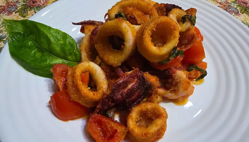 Anelli di calamari croccanti e pomodorini cotti nella friggitrice ad aria, guarniti con una foglia di basilico.