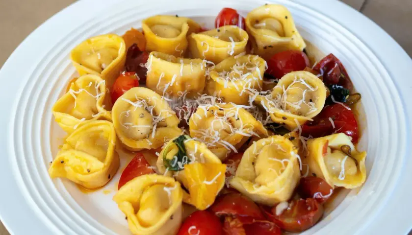 Domowe tortellini z mięsem, pomidorkami i parmezanem na białym talerzu.