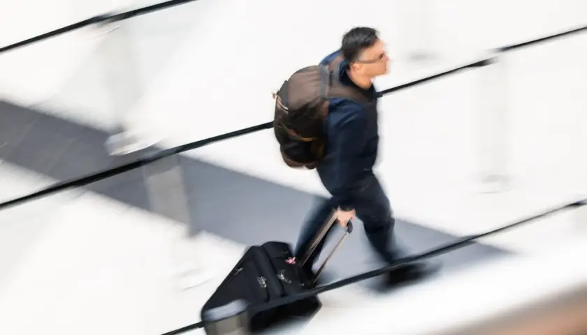 Mężczyzna z plecakiem i walizką na kółkach w ruchu.
