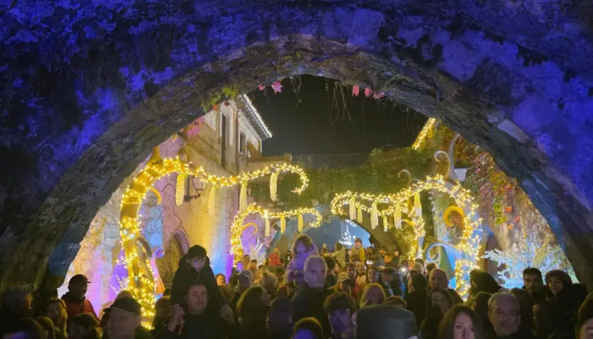 Gente disfrutando del mercado navideño en Cartes, con luces brillantes y ambiente festivo bajo un arco de piedra.