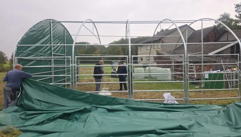 Aufbau einer 100 qm Halle genehmigungsfrei in Bayern. Männer montieren das grüne Dach einer Leichtbauhalle.