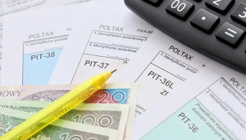 Zestaw dokumentów PIT, kalkulator, żółty długopis i polskie banknoty. Czas na rozliczenie zap-3.