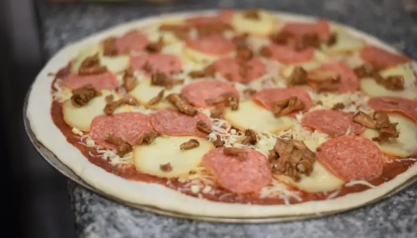 Gotowa do pieczenia pizza z salami, mozzarellą i grzybami. Idealna na kolację po włosku.