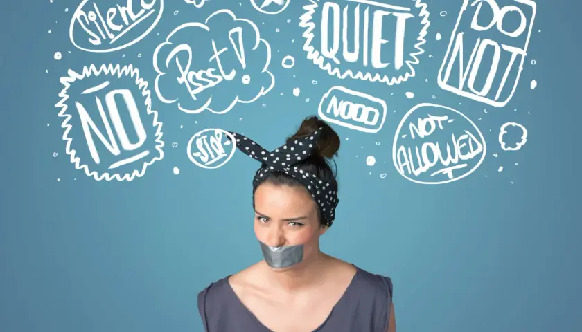 Kobieta z zaklejoną taśmą ustami, otoczona chmurkami z napisami "Silence", "Quiet", "No", "Stop", symbolizującymi tłumienie emocji.