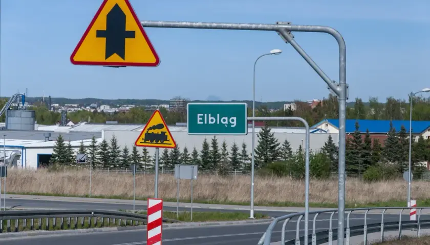 Uwaga na skrzyżowanie z drogą podporządkowaną i przejazd kolejowy. Znak "Elbląg" zaprasza do miasta.