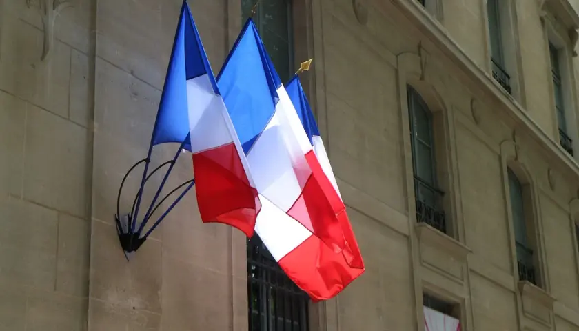 Trzy flagi Francji powiewają na tle kamiennej fasady budynku. Francuski to język urzędowy w wielu krajach, nie tylko w Europie.