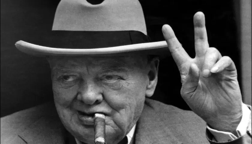 Winston Churchill, chapeau, cigare et signe de victoire. L'alcool et le cigare font partie de son image iconique.