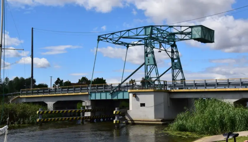 Most czterech pancernych, podnoszony most nad kanałem, z zieloną konstrukcją i błękitnym niebem.