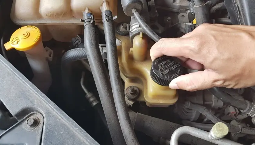 Ręka zakręca korek zbiorniczka płynu wspomagania kierownicy. Wymiana płynu wspomagania to ważny element dbania o auto.