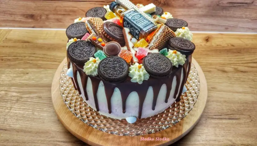 Tort z polewą czarny drip, ozdobiony ciasteczkami Oreo, waflem i mini buteleczką Jack Daniel's.