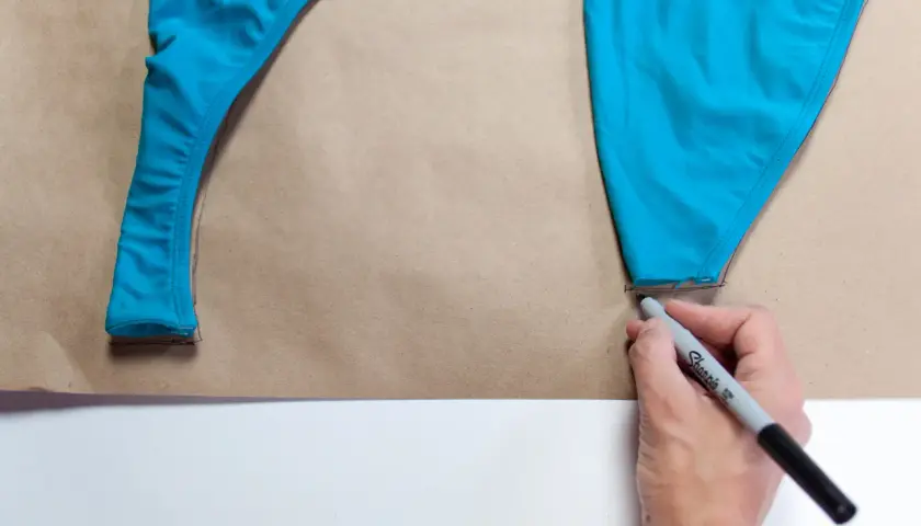 Tracing a blue swimsuit piece onto brown paper, a step in how to make a swimsuit.