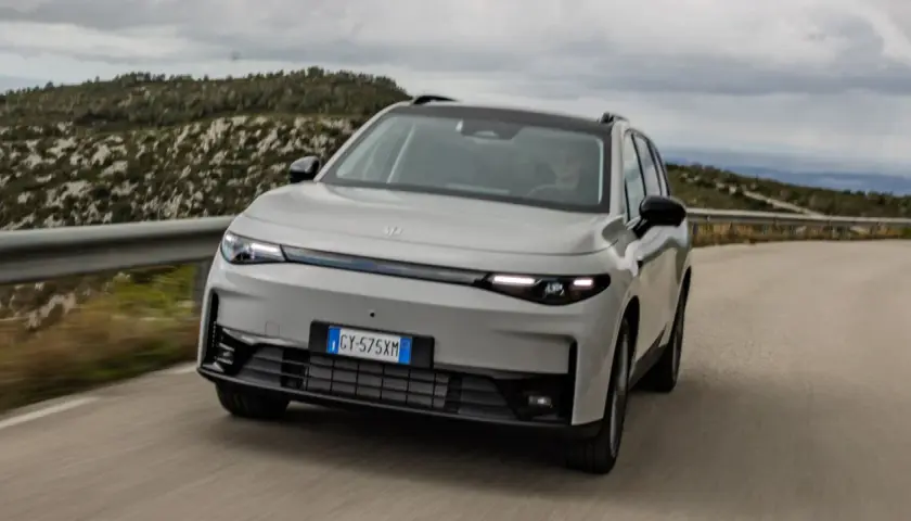 Leapmotor C10 REEV in grigio chiaro sfreccia su una strada panoramica, con un guidatore al volante.