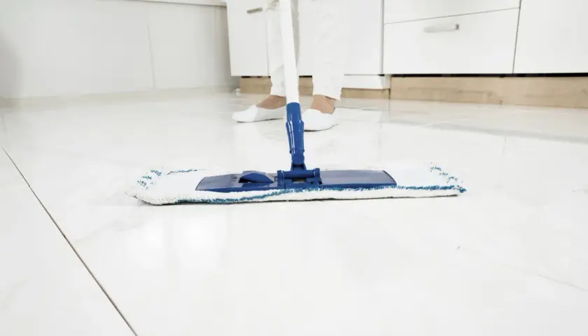 Pulizia finale del pavimento bianco dopo la ristrutturazione. Un mocio pulisce le piastrelle lucide, lasciando una finitura impeccabile.