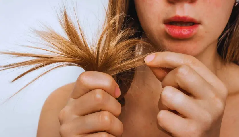 Una mujer examina su pelo seco, notando las puntas abiertas y la falta de brillo.