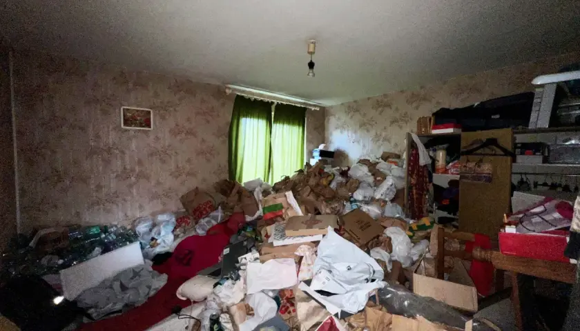 Un logement insalubre envahi par des montagnes de sacs et de détritus. La pièce est encombrée, rendant la circulation difficile.