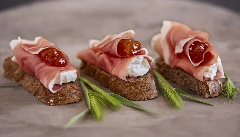 Drei kleine Brote mit Frischkäse, Feigenmarmelade und Schinken – so sieht ein köstliches Crudo aus.