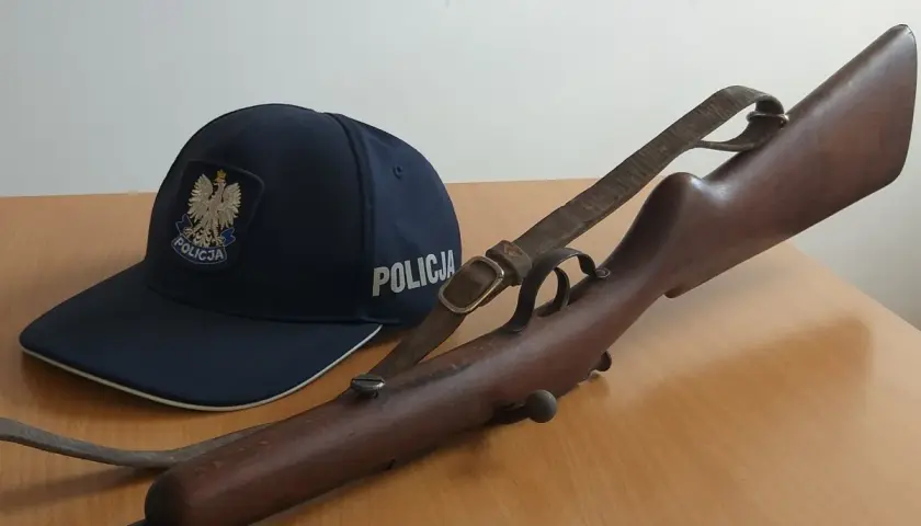 Policyjna czapka i karabin, prawdopodobnie kbks bez pozwolenia, leżą na drewnianym stole.