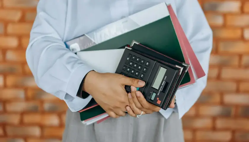 Osoba trzyma stos dokumentów i kalkulator. Idealne do usług fotograficznych, gdzie liczy się każdy szczegół, także VAT.